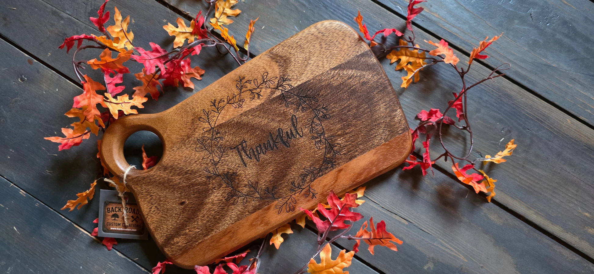 Wooden cutting board with 'Thankful' engraving on a wooden surface with autumn leaves.